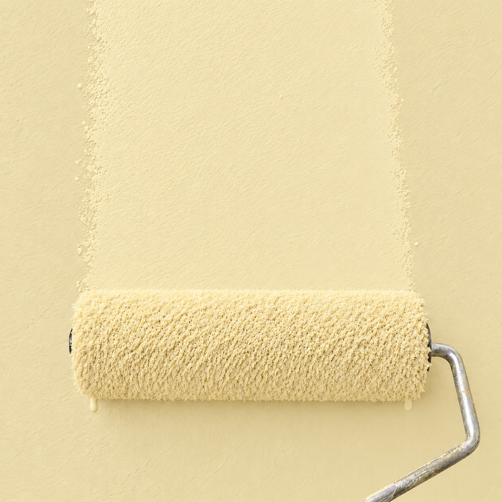Paint roller spreading Butter Glen soft butter yellow paint across a matching wall.