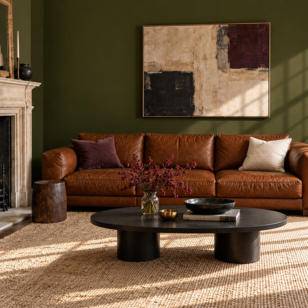 Garden Armory dark olive green living room walls with a tobacco leather sofa and black oval coffee table.