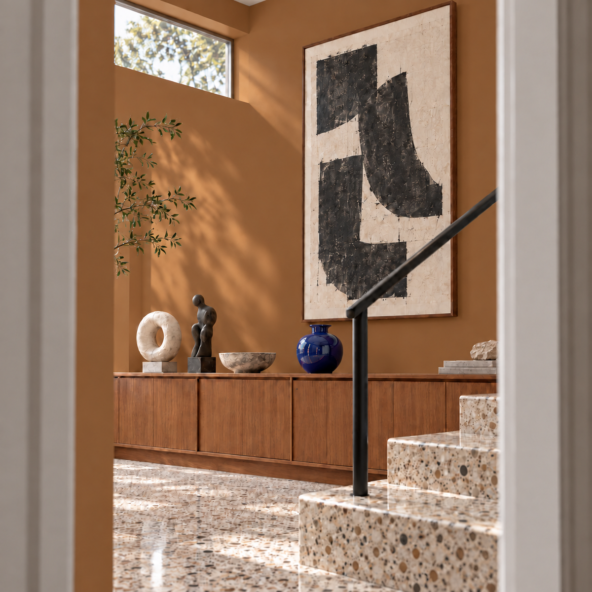 Mid-century gallery entryway with Ochre Saddle warm ochre brown walls, graphic artwork, a cobalt vase, teak cabinetry, and terrazzo stairs.