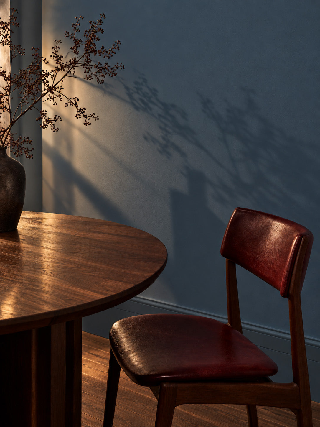 Tempest Slate slate blue-gray dining room wall with a walnut table, oxblood leather chair, and branch shadows