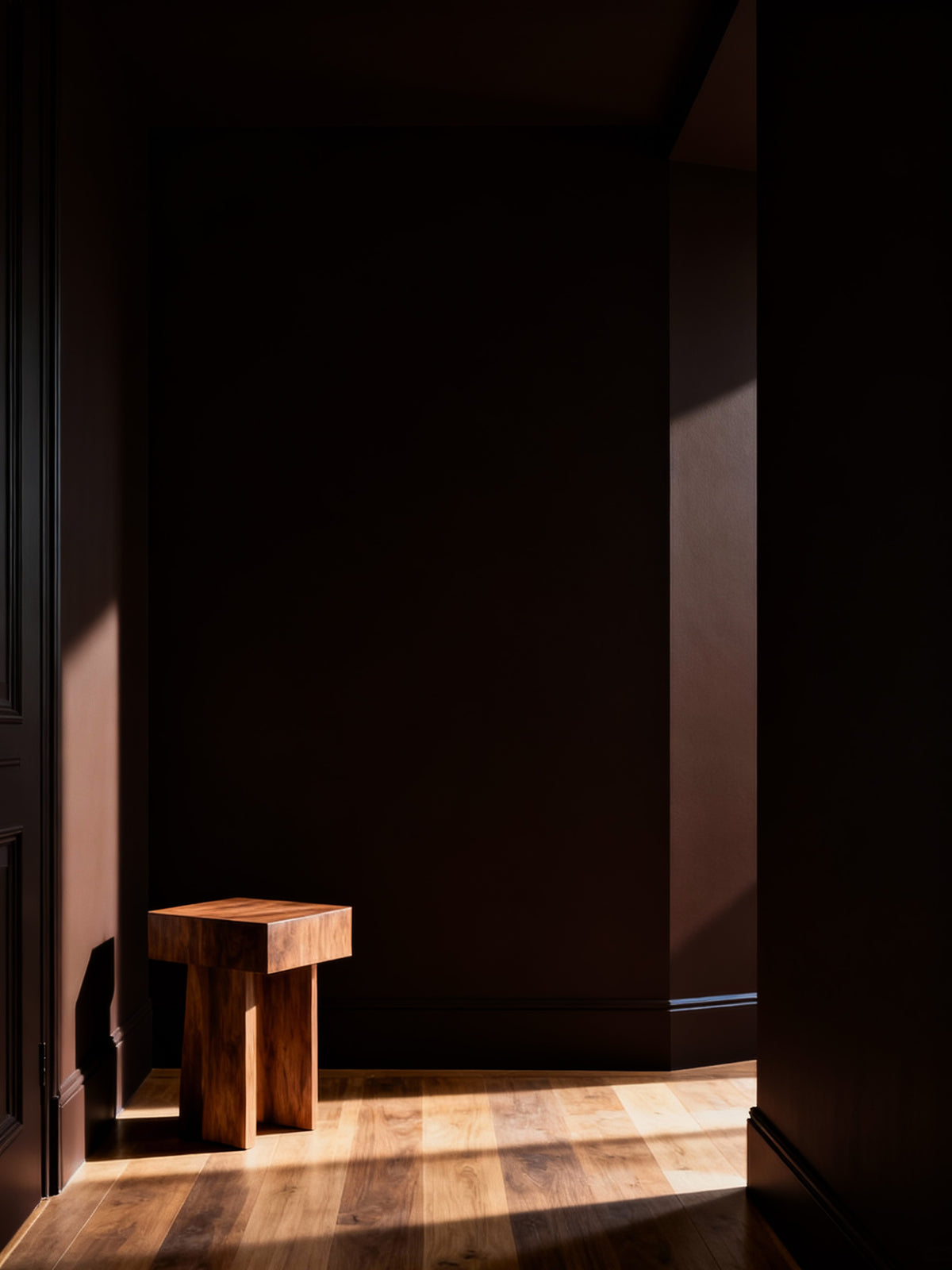 Wooden stool in a dimly lit room with sunlight casting shadows on the wall.