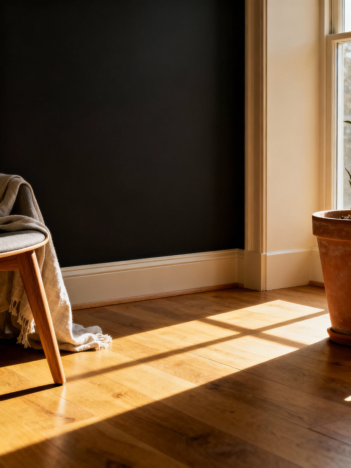 Sunlight streaming through a window onto a wooden floor with a black wall and a chair.